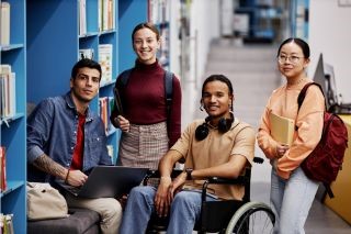 Diverse group of students with young man in wheelchair looking at camera in library.